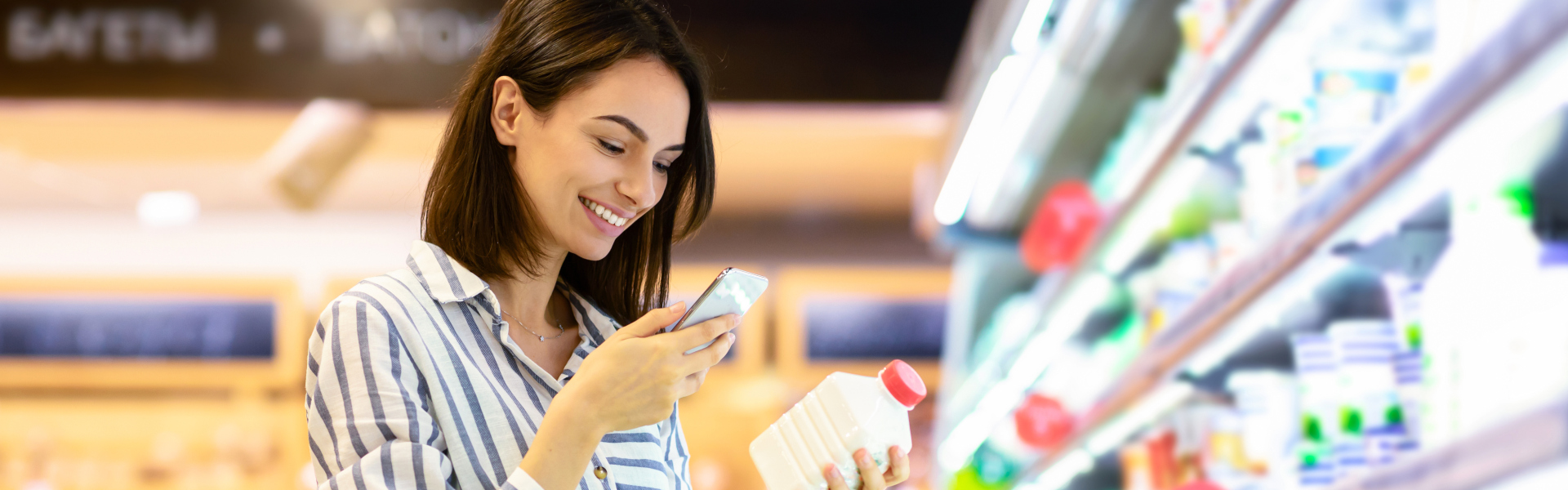 Frau im Supermarkt scannt mit dem Smartphone ein Produkt und lächelt dabei.